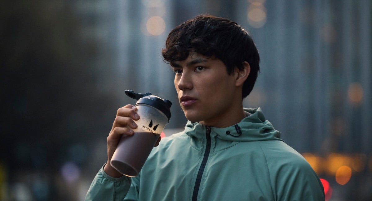 A man drinking a Myprotein protein shake on a city street