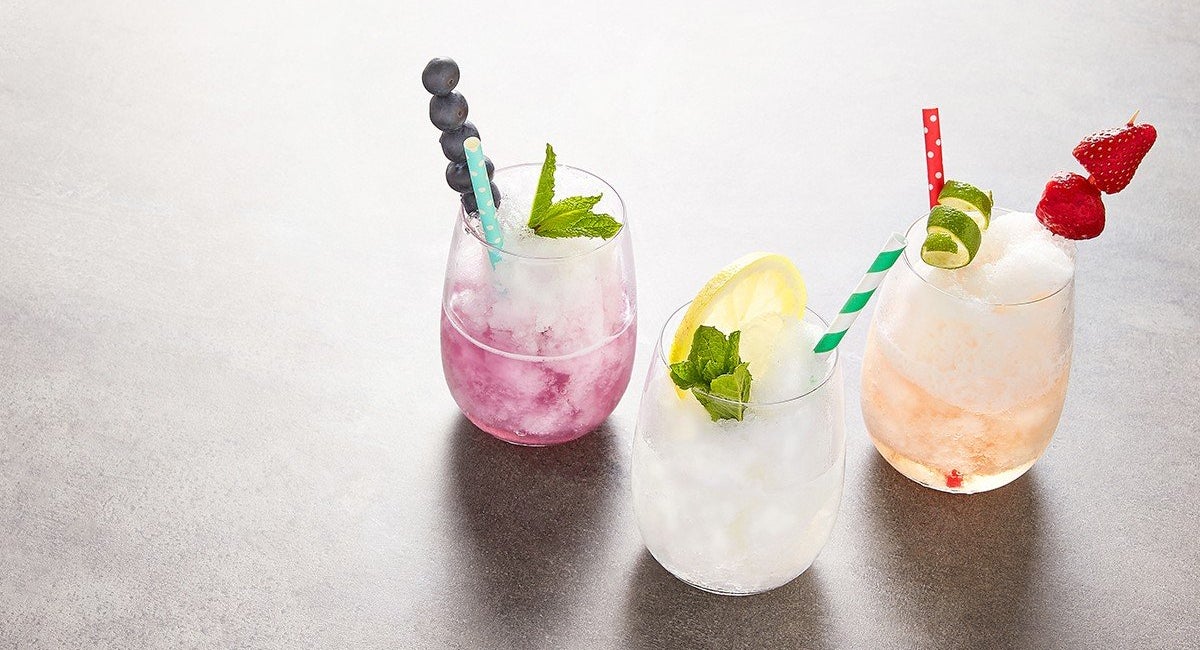 Three clear protein slushies in glasses, garnished with fruit and mint