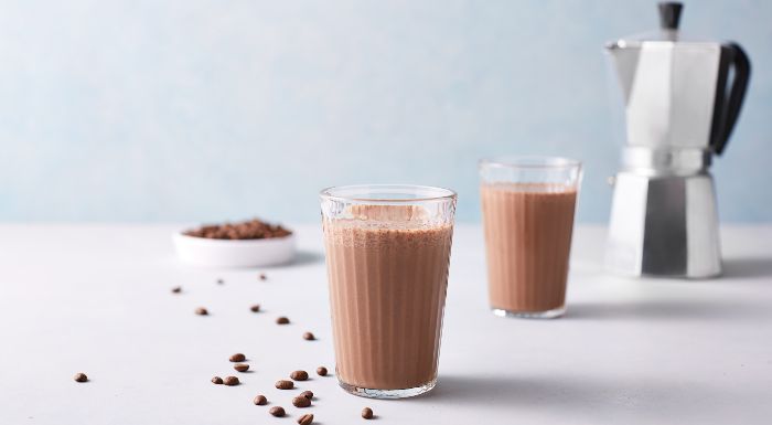 Two glasses of iced coffee protein shake, with coffee beans and a moka pot