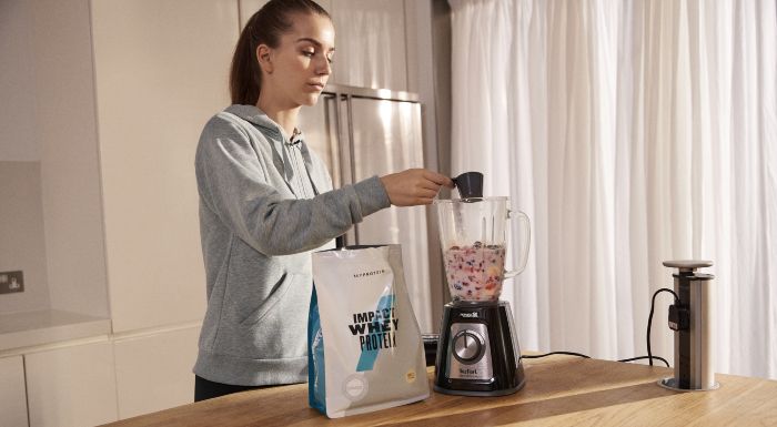Woman adding a scoop of Myprotein Impact Whey Protein to a blender