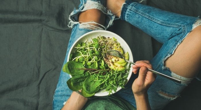 Person holding a bowl of salad greens, avocado and sprouts