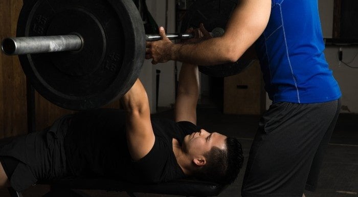 Man doing a barbell bench press with a spotter