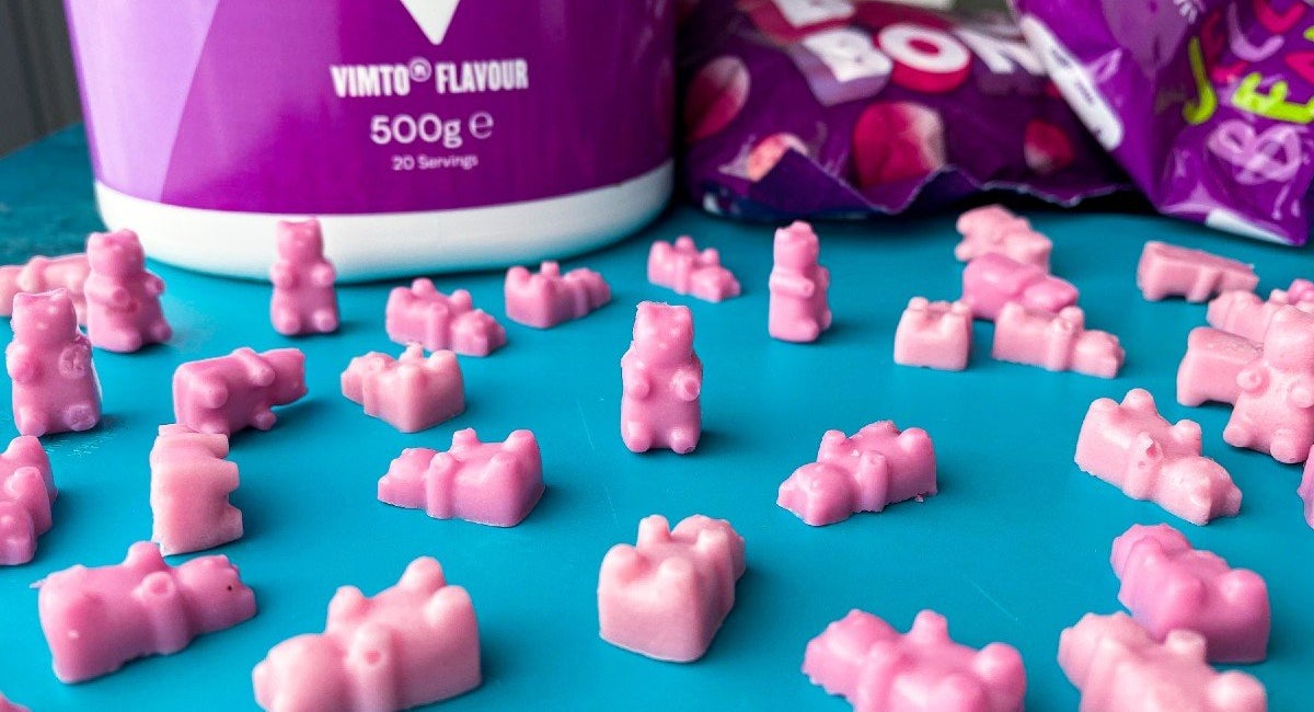 Pink Vimto Clear Whey gummy bears in front of a tub of Vimto Clear Whey Isolate