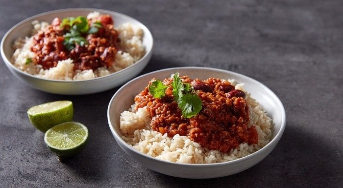 Two bowls of vegan chilli with rice and lime