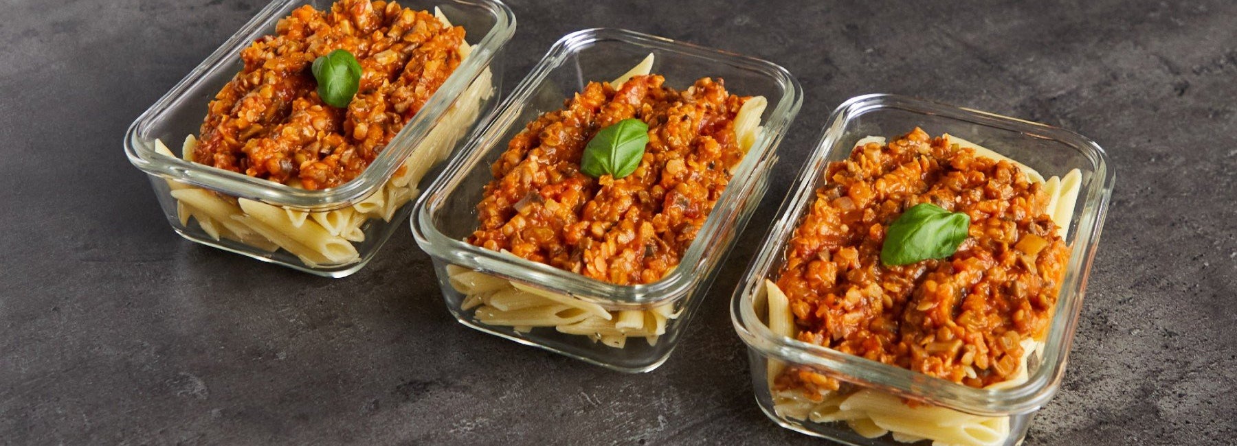 Three meal prep containers of vegan lentil bolognese with pasta