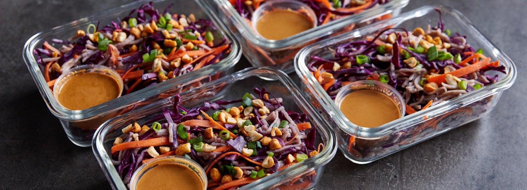 Four meal prep containers of cold peanut noodle salad with dressing