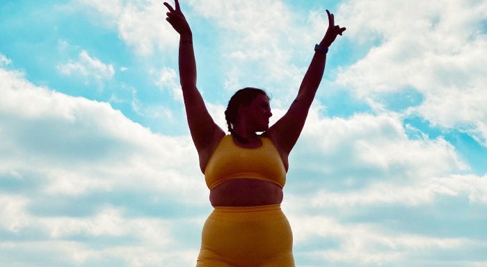 Woman in a yellow sports bra raising her arms against a blue sky