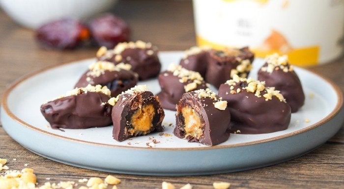 Chocolate-coated peanut date bars on a plate, one cut open