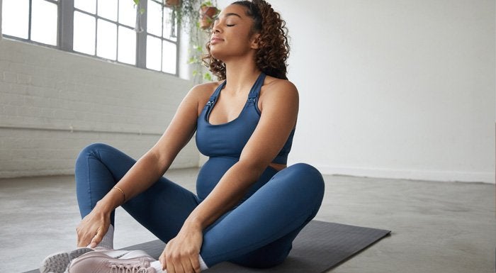 Pregnant woman sitting cross-legged on a mat with her eyes closed
