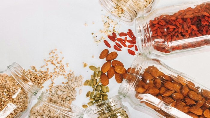 Jars of nuts, seeds and goji berries spilling onto a table
