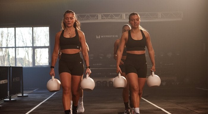 Women doing a farmers carry with kettlebells at a HYROX event