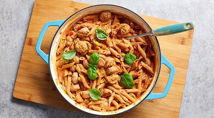 Creamy sausage pasta with basil in a blue casserole dish