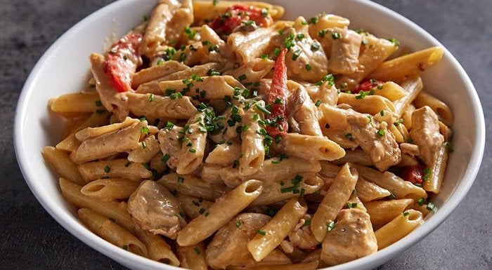 Bowl of creamy Cajun chicken penne pasta with peppers and chives