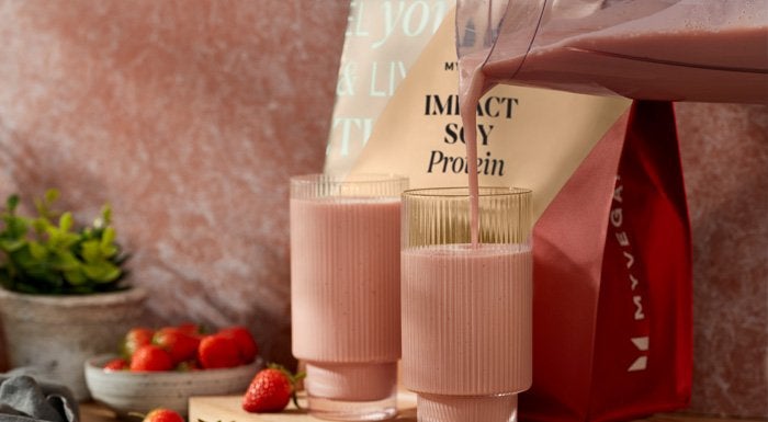 Strawberry shake being poured into glasses next to a pouch of Impact Soy Protein