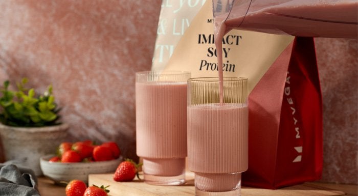 Strawberry shake being poured into glasses next to a pouch of Myvegan Impact Soy Protein