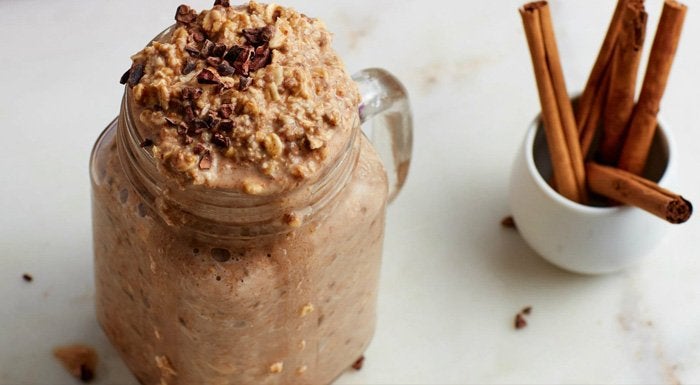 Cinnamon overnight oats in a glass jar, next to cinnamon sticks