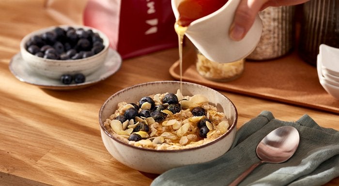 High-protein porridge topped with blueberries and seeds, with syrup being poured