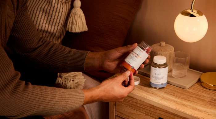 Person taking supplements from a bottle on a bedside table