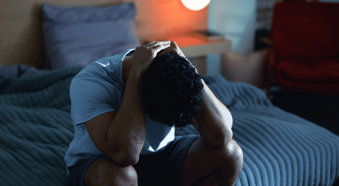 Man sitting on the edge of his bed with his head in his hands