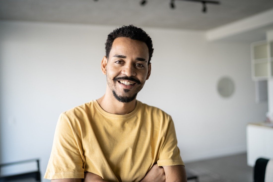 A man with a goatee and moustache smiles wearing a yellow t-shirt | Gillette UK