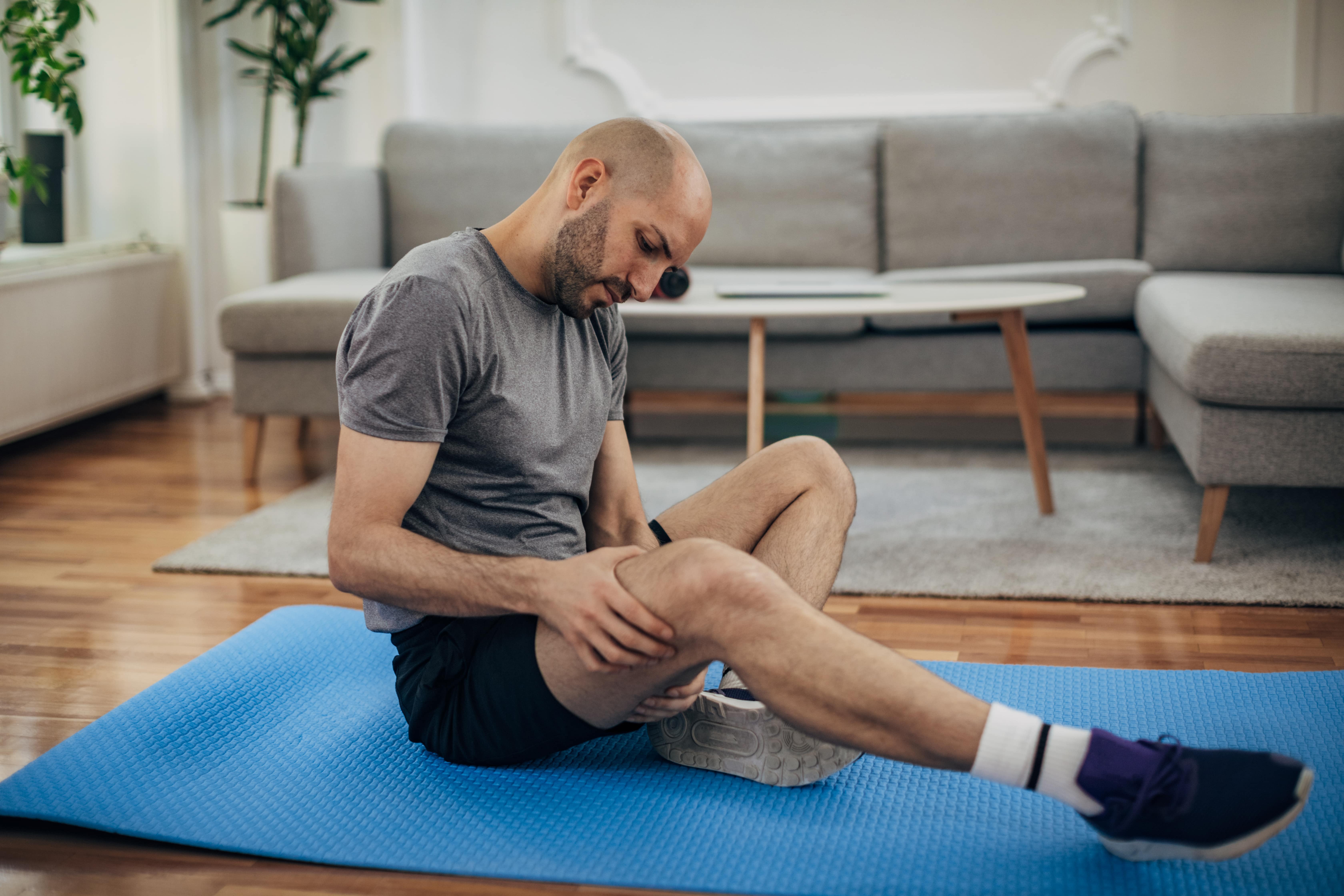 A man sits on a blue yoga mat holding his thigh | Gillette UK