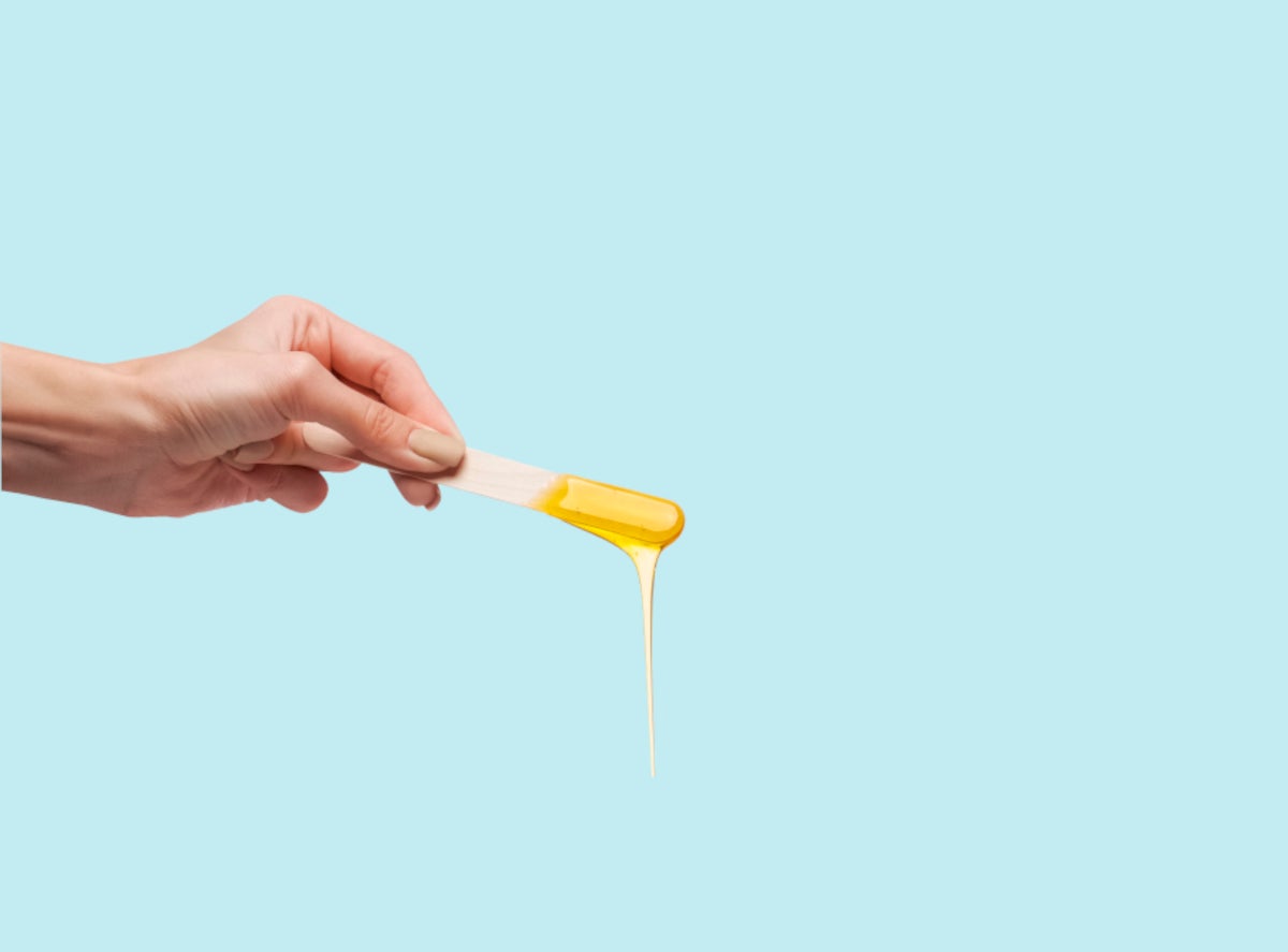 A hand holds a stick with hot wax dripping from it against a pale blue background | Gillette Venus UK