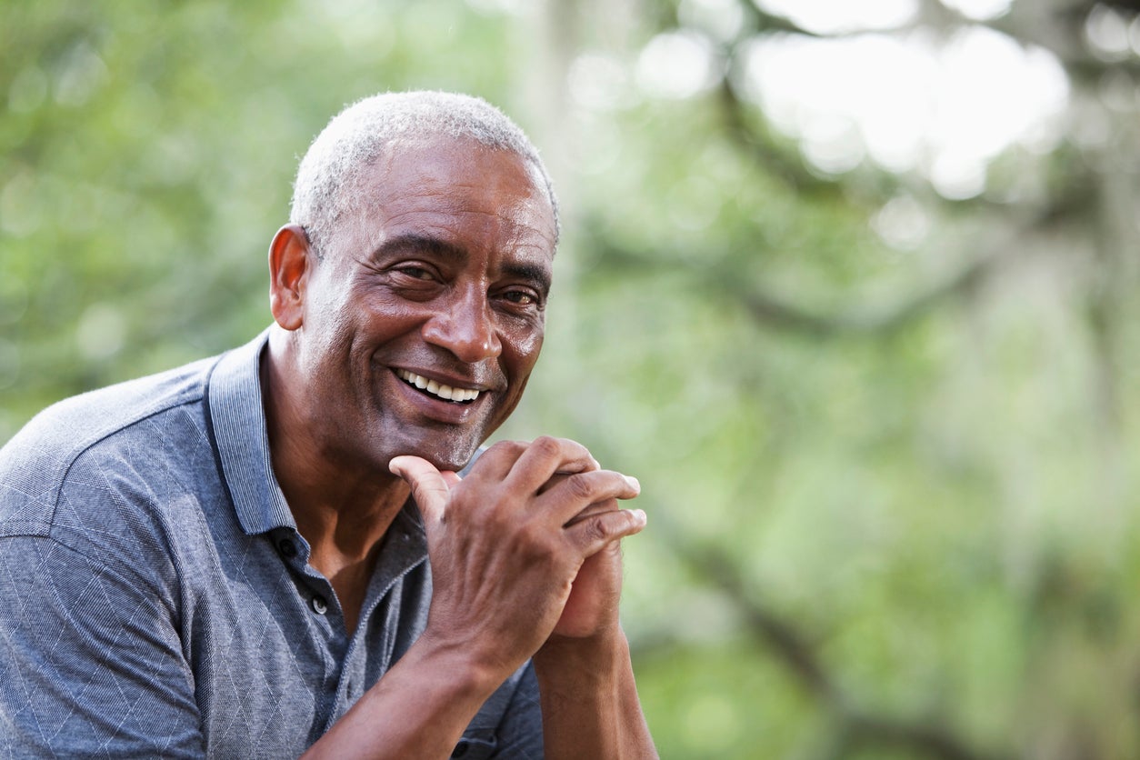 Man with grey buzzcut hairstyle smiling while resting his chin on his hands