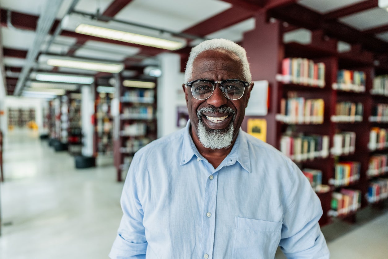 Man with short grey hair, a goatee, and glasses smiling confidently at the camera in a library.