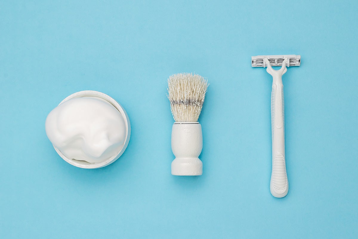 A white pot of shaving foam, shaving brush and a razor against a pale blue background | Gillette Venus UK