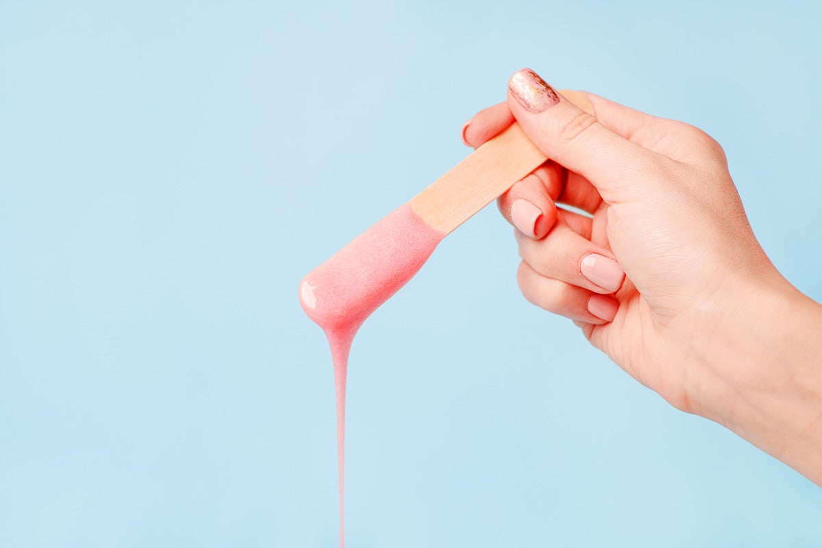 A hand holds a stick with hot wax dripping from it against a pale blue background | Gillette Venus UK